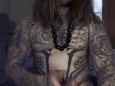 Long-haired, heavily inked beefy muscle hunk plays with his huge uncut cock